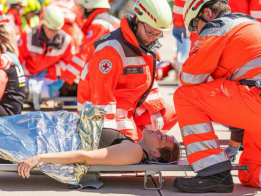 Einsatzübung von DRK und Feuerwehr auf dem Flughafen von Dresden: Rettungskräfte vom DRK versorgen eine Frau, die auf einer Trage liegt 